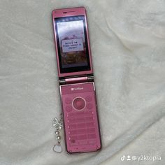 a pink cell phone sitting on top of a white sheet with a keychain