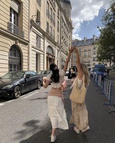 two women walking down the street with their arms in the air