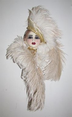 a white doll with feathers on it's head is wearing a gold and white costume