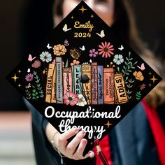 a woman holding a graduation cap with books on it and flowers in the background that reads,