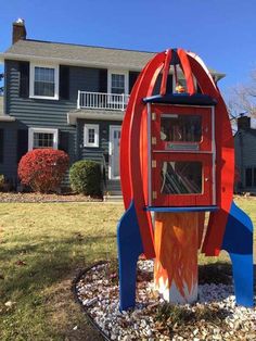 a red and blue rocket ship shaped mailbox in front of a house