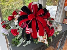 a christmas wreath with red and black ribbons on a table in front of a window