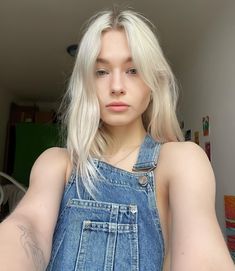 a woman with blonde hair and blue overalls is posing for the camera in her bedroom