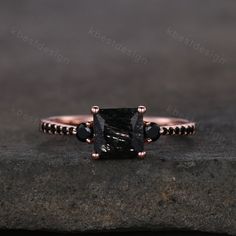 a black diamond engagement ring on top of a stone slab with beading around the band