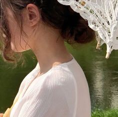 a woman standing in front of a body of water wearing a white lace head piece