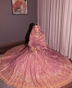 a woman in a pink and gold wedding dress sitting on the floor next to a window