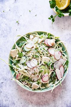 a salad with radishes and onions in a green bowl on a marble surface