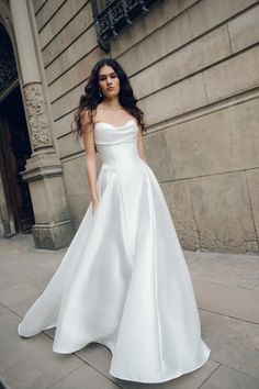 a woman in a white dress is standing on the sidewalk