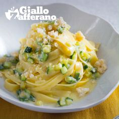 a white bowl filled with pasta covered in sauce and vegetables on top of a yellow table cloth