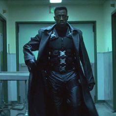 a man dressed in black leather is walking down the hall with his hands on his hips