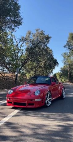 a red sports car parked on the side of the road in front of some trees