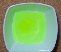 a white bowl with green liquid in it on a brown counter top next to a black object