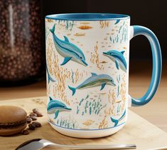 there is a coffee cup with dolphins on it next to a spoon and some nuts