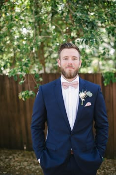 a man with a beard wearing a blue suit and bow tie standing in front of a fence