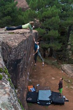 two people standing on the edge of a cliff with their arms in the air and one person laying down