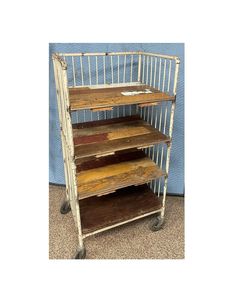 an old metal and wood shelf with three shelves on wheels, in front of a blue wall