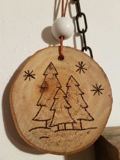 a wooden ornament with a christmas tree drawn on it hanging from a chain