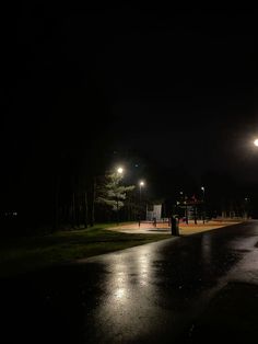 an empty street at night with lights shining on the ground and trees in the background