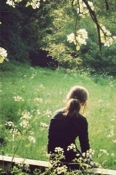 a woman sitting on a bench in the middle of a field with wildflowers