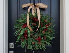 a wreath with pine cones and red berries hangs on the front door's black door