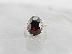 This ring features a simple and classically designed mounting, sized perfectly for a cocktail piece! The structural pattern of the shoulders lends a sense of light and grace to the mounting. Shaped in a perfect oval, the deep red of the garnet in the center adds a lovely pop of color to a simple but classic ring! Metal: 14K Yellow Gold Gem: Garnet 13.82 Carats Gem Measurements: 11.9 x 15 mm, Oval Ring Size: 5 Vintage Garnet Ring, Garnet Ring Vintage, Yellow Gold Sapphire Ring, Pyrope Garnet, Demantoid Garnet, Vintage Cocktail Ring, Oval Ring, Garnet Ring, Oval Rings