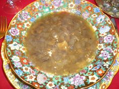 a bowl of soup is sitting on a plate next to a fork and glassware