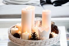 candles and pine cones are arranged in a basket on a coffee table with other decorations