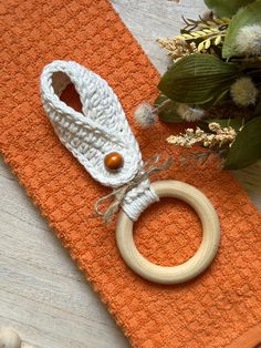 a knitted ring sits on an orange placemat next to a flower and leaves