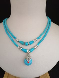 a necklace with two blue beads and a silver pendant on a white mannequin