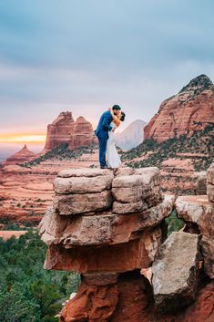 a bride and groom kissing on top of a rock formation in the desert at sunset