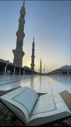 an open book sitting on top of a floor in front of a tall building with two minarets