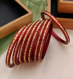 red and gold bangles are sitting on a table next to a wooden box with an empty