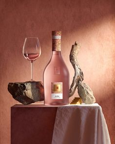 a bottle of wine next to a glass on a table with rocks and a piece of driftwood