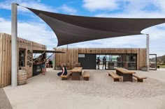 an outdoor play area with benches and tables under a large shade sail over it's entrance