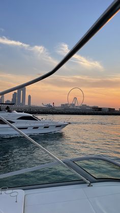 the sun is setting behind two boats in the water near an amusement park and ferris wheel