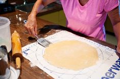 an older woman is making pizza dough with a fork and knife on a cutting board