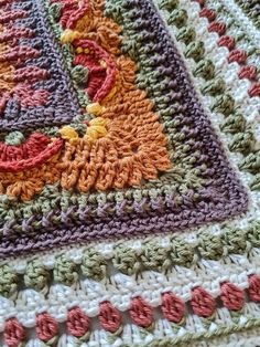 a crocheted blanket is laying on top of a tablecloth that has been made with multicolored yarn