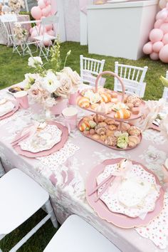 a table set up with pink and white plates, napkins, flowers and desserts