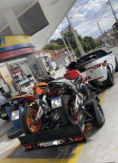 two motorcycles are parked next to each other at a gas station with cars in the background