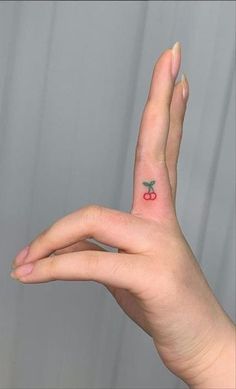 a person's hand with a small tattoo on the middle finger and an apple in the middle