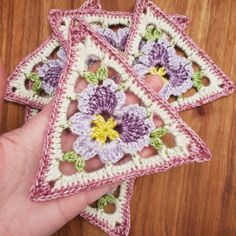 a hand is holding three crocheted coasters with flowers on them, one in the shape of a star