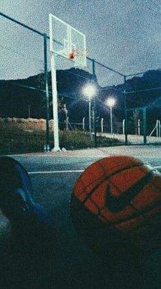 two basketballs sitting on the ground in front of a basket ball and some lights