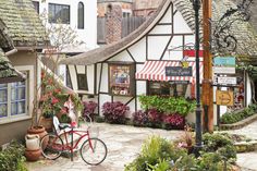 a red bike parked in front of a building with flowers on the outside and an awning over it