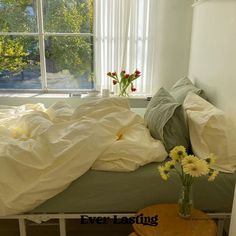 an unmade bed with white sheets and flowers in a vase on the end table