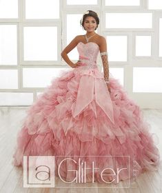 Make grand entrance in this ruffled strapless ball gown by House of Wu LA Glitter 24011 during your Quinceanera, Sweet 16 party, or for any formal event. Gape at the shining array of glitter tulle and iridescent organza; a complete ruffled ball gown with the added accessory of a removable train attachable via velcro. The bodice organza gathers to one side and is plastered with a magnificent applique of rhinestones and shiny metallic thread. Complete with a large organza bow and lace up back. ... Charro Dress, Iridescent Organza, Quince Dress, Disney Princess Dresses, Princess Ball Gowns, Ruffled Dress, Ruffled Skirt, Glitter Dress, Quince Dresses