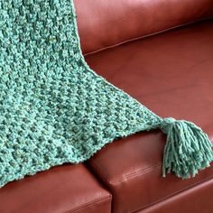 a green crocheted afghan sitting on top of a brown leather couch next to a pillow