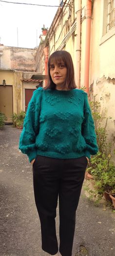 a woman standing in the middle of an alley way wearing a green sweater and black pants