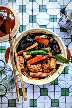 a large bowl filled with lots of food on top of a table next to chopsticks