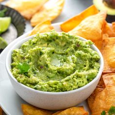 guacamole in a white bowl surrounded by tortilla chips and avocado