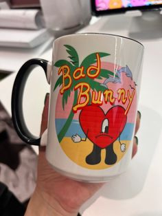 a person holding up a coffee mug with the words bad bunny on it in front of a computer screen